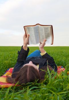 Teen girl reading the Bible outdoors at sunset time