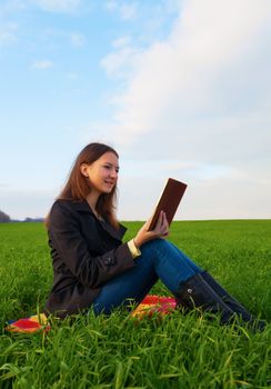 Teen girl reading the Bible sitting outdoors at sunset time