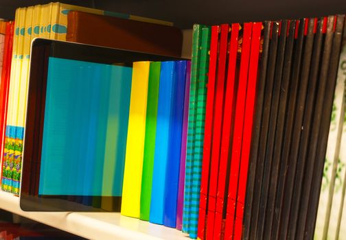 Row of colorful books and electronic book reader on the shelf