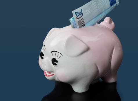A single twenty euro bill inserted into the slot on a piggy bank with blue reflection
