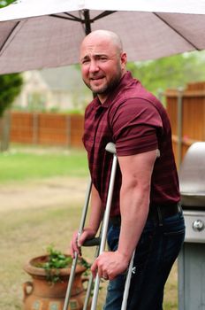 Muscular bald man on crutches looking at camera.