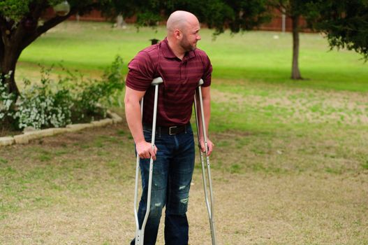 Muscular bald man on crutches outdoors.