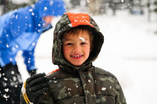 Little boy out in the snow smiling at camera.