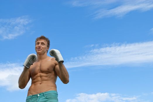 Young guy in boxing gloves training outdoors under the blue sky.
