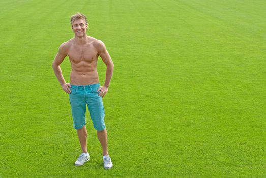 Fit young man standing on green playing field, smiling.