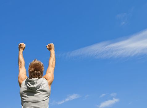 Sporty guy with his arms raised in joy, on blue sky background.