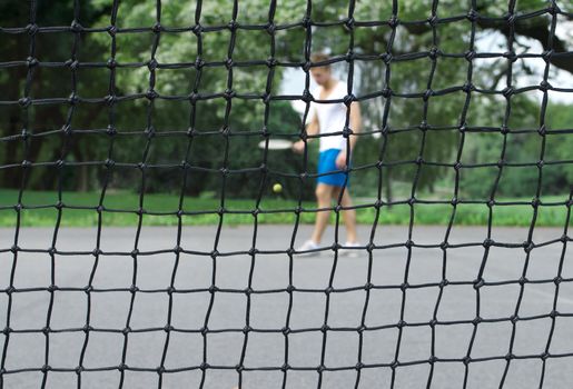 Tennis player with racket and ball seen through the tennis net. Focus on the net.