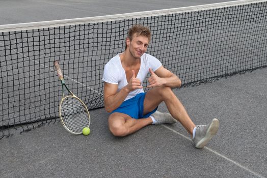 Tennis player sitting besides the net and showing thumbs up.