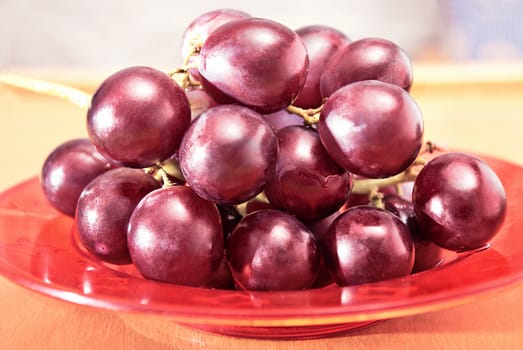 Closeup fresh grapes on the plate on a wooden table.
