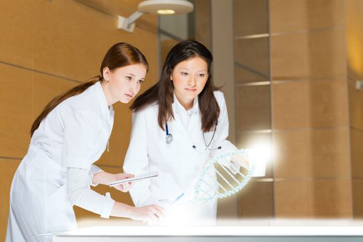 two doctors stand near glowing table discussing. projected objects on a desk