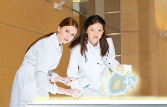 two doctors stand near glowing table discussing. projected objects on a desk