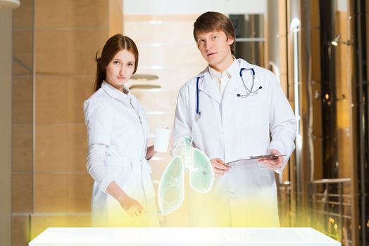 two doctors stand near glowing table discussing. projected objects on a desk