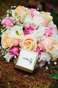 wedding bouquet of roses and pair rings lying of forest coniferous ground