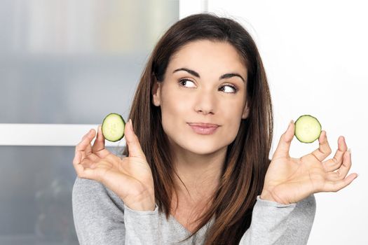 Woman with a slice of cucumber in kitchen