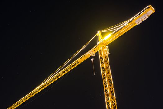 Construction crane at night brightly lit against stary sky