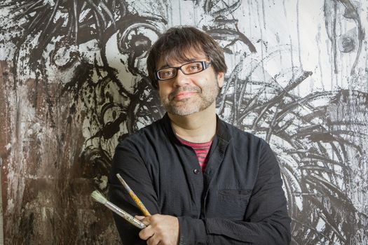 Painter artist with black glasses posing in front of his mural paint