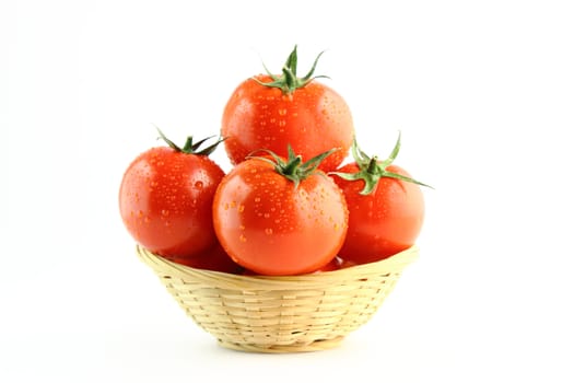 fresh tomatoes with green leaves and water drops in a basket of straw.