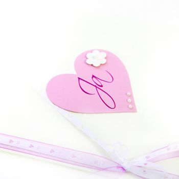 Pretty pink paper Valentines heart and bow decorated with a flower and bearing the handwritten word Ja