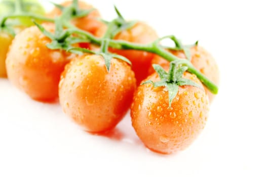 fresh cherry tomatoes with water drops and green leaves on white background