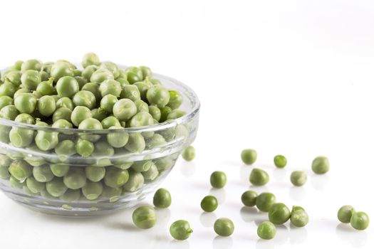 Fresh green peas in a glass bowl and on white surface.