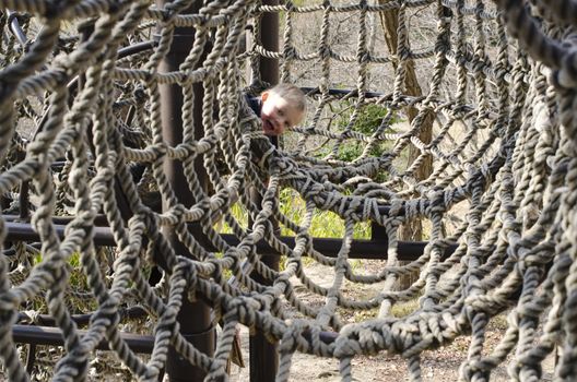 Young boy looking around the corner in a climbing net