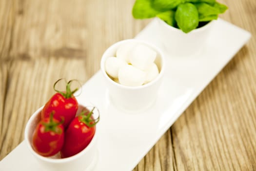 tasty tomatoes mazarella and basil on plate on wooden background