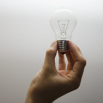 A human hand holding an incandescent light bulb. White backgound.