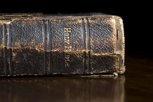 Selective focus on the Antique Holy Bible Spine on wooden table with black background