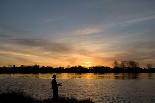 Man fishing from the river's edge at sunrise