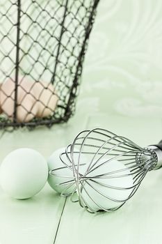 Fresh free range Ameraucana eggs in a whisk with brown eggs in a vintage basket in background. 
