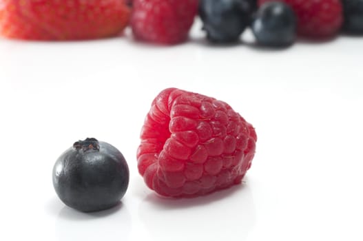 Selective focus on a single blueberry and raspberry isolated on white with more berries in the background