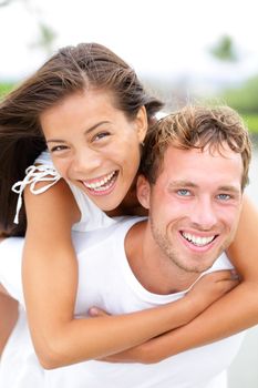 Couple happy having fun piggybacking and laughing outdoors during summer holidays travel vacation. Happiness concept with interracial couple, Asian woman and Caucasian man.