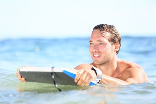 Beach fun - man bodyboarding on bodyboard smiling happy surfing on boogieboard during holidays beach travel. Young handsome Caucasian male beach model joyful outside doing water sport.