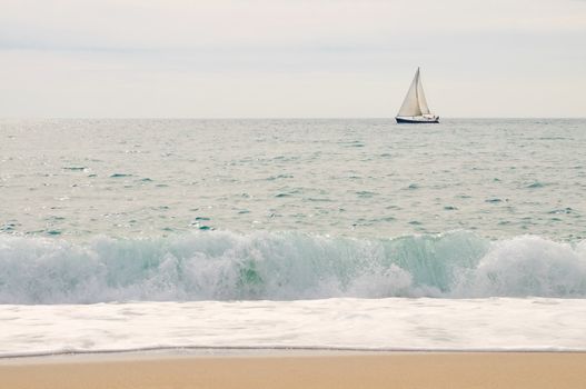 Freedom. Only one yacht on the open sea with waves and beach in foreground