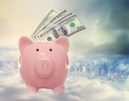 Piggy bank with us dollar bills on a cloud above the city