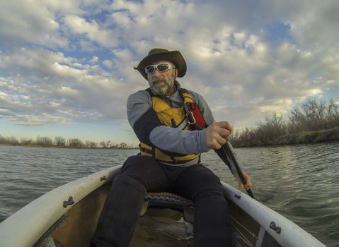 senior male paddling a canoe on calm lake in early spring in Fort Collins, Colorado, POV shot from a boat bow