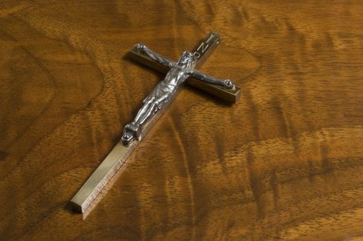 Metal Christian cross on antique wood grain table top.
