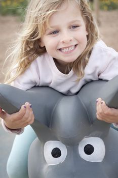 Close up of a child on a rocking horse in a playground. She is looking sideways, smiling. Real people