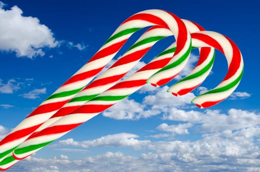 Three sugar sticks in white green and red on background of sky and clouds