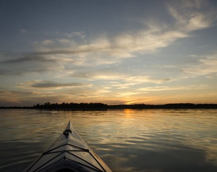 Kayak on the lake with the treeline and sunset in the background. This is a compsite image using two horizontal images placed together