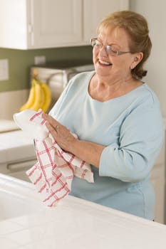 Smiling Senior Adult Woman Drying Bowl At Sink in Kitchen.