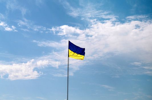 Flag of Ukraine with flag pole waving in the wind on front of blue sky