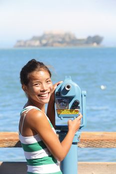 San Francisco travel tourist looking at Alcatraz Island prison with tourist binoculars. Multicultural woman looking happy at camera. California tourism concept.