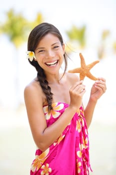 Summer vacation woman smiling happy holding starfish on Hawaiian beach. Cute multicultural Asian Caucasian female model joyful and adorable in red pink sarong