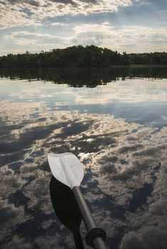 Sunrise peaking through the clouds and reflecting on the calm lake with a kayak paddle in the foreground