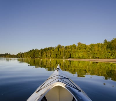 Kayak on a tranquil lake with reflection of shoreline beach area and forest in a northern park