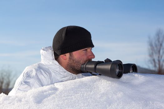 Scout in white camouflage coat with binoculars on white snow