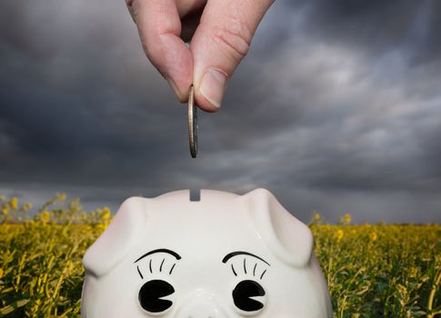 Coin being inserted into piggy bank with fingers suggesting saving for a rainy day or stormy weather