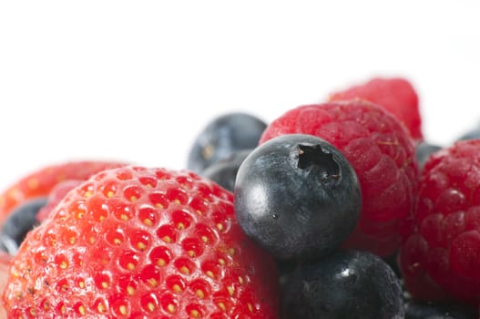 Macro image with selective focus on a strawberry, blueberry and raspberry in the foreground with more fruit in the background with copy space at the top with white background.
