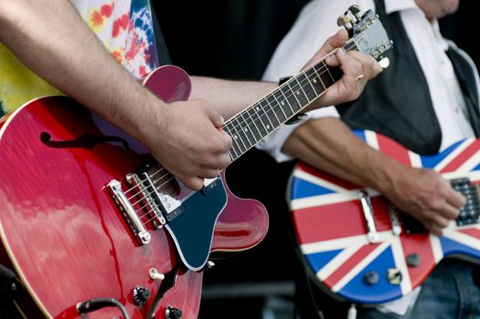 Two rock and rollers at a music festival with selective focus on the forground hands strumming the guitat